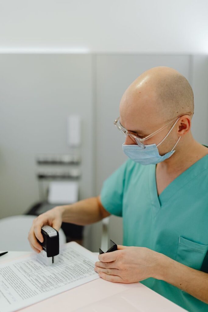 Healthcare professional wearing scrubs and mask reviewing documents at a desk indoors.